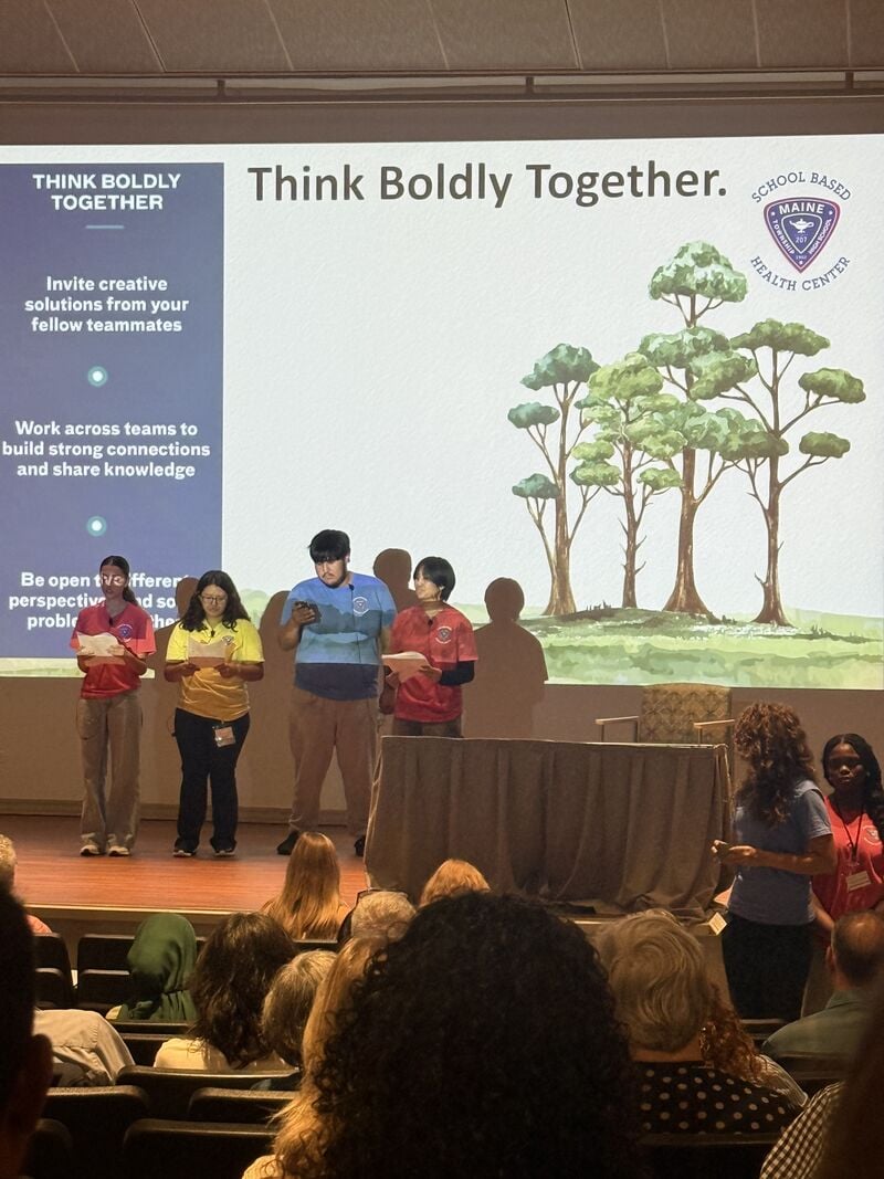 Presenters on stage in front of a slide reading Think Boldly Together